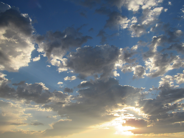 rays of sun shining upward toward the clouds in the blue sky