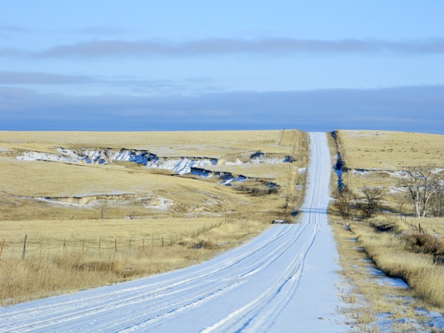 snow covered gravel road in Nebraska against the golden pasture grass